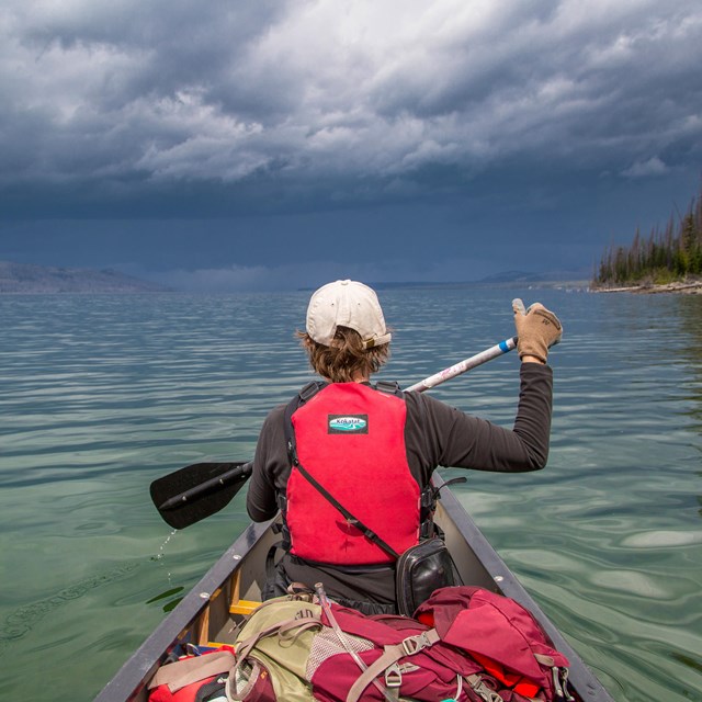 a boy in a lifejacket paddles a canoe on a lake