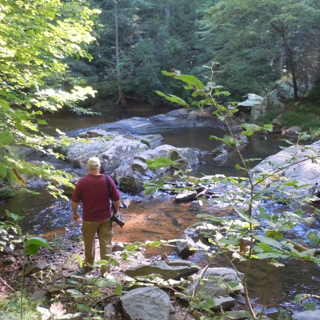 Hiker with a camera next on the rocks of the Quantico Creek