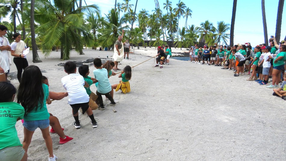 School children compete in huki huki (tug-of-war) as others cheer them on.