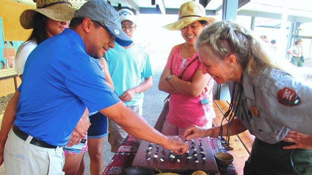 A Ranger teaches visitors how to play kōnane (Hawaiian checkers)