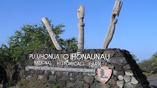 Puʻuhonua o Hōnaunau National Historical Park sign with three carved kiʻi images