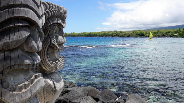 Two carved wooden images (ki'i) with the ocean beyond. Photo by John Wilcart