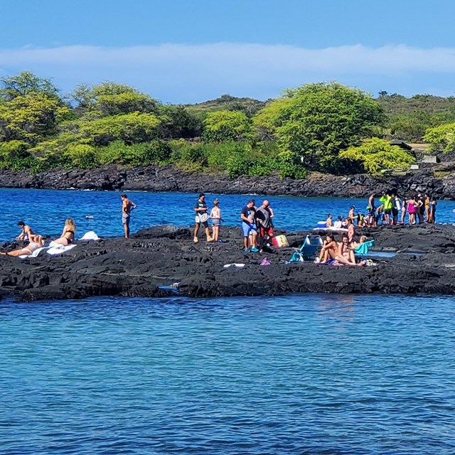 People gather on black lava rock at the popular snorkel spot, 