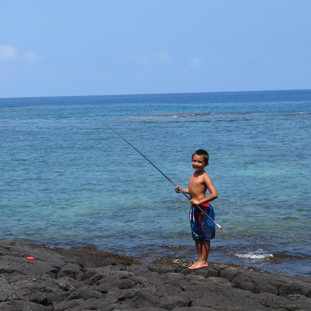 Three young fishermen pose with their fishing poles at the water's edge