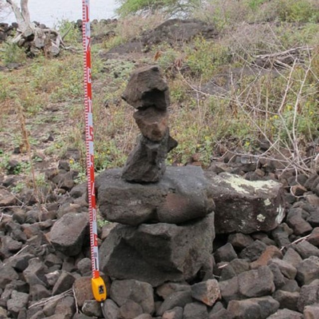 A stacked rock cairn with measuring tape next to it.