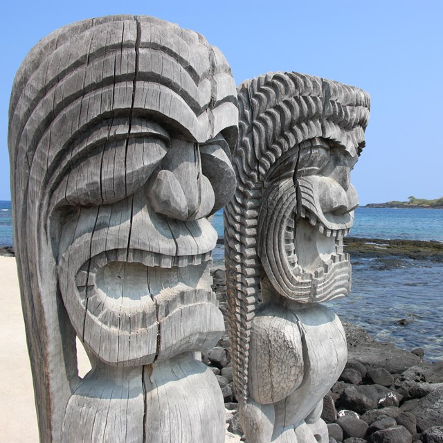 Two carved kiʻi images look out over the ocean