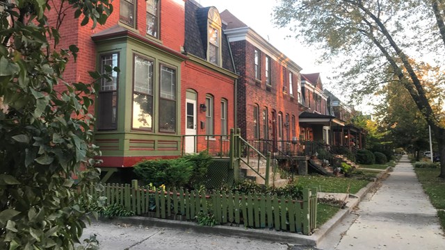 A photo of Pullman brick rowhouses in the fall with fall trees and various floral landscapes.