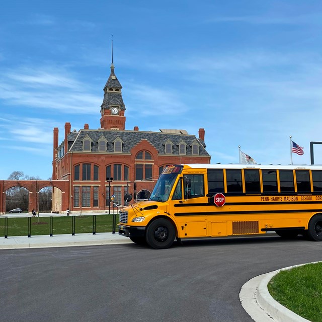 A school bus sits in a parking lot in front of the red bricked administration clock tower building.