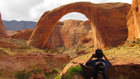 A person has his back to Rainbow Bridge as he takes a picture.
