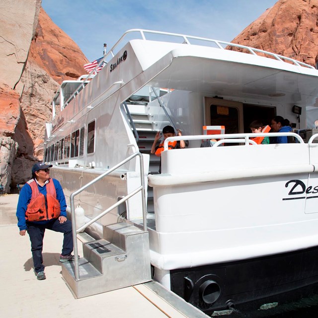 Captain stands on dock with one leg perched on steps leading to large tour boat