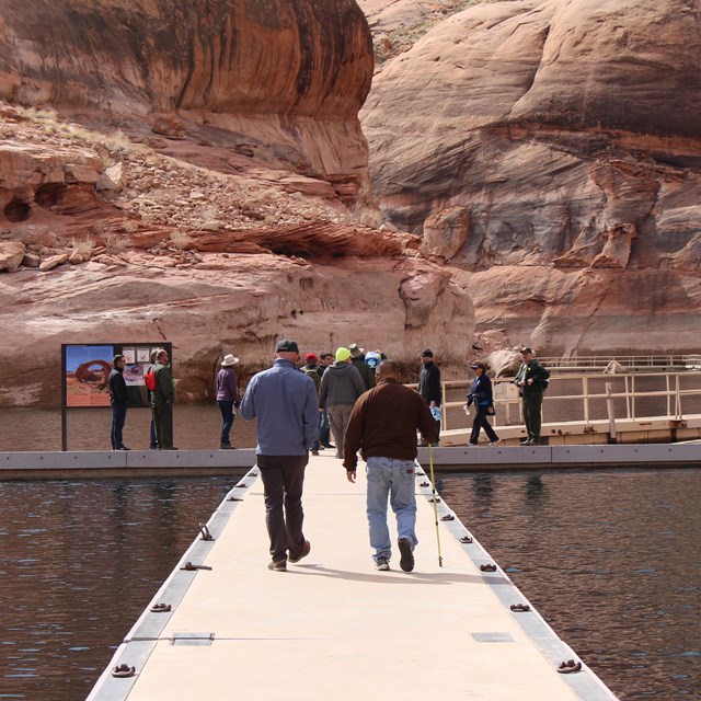 A man with a cane walks down floating walkway alongside another visitor 