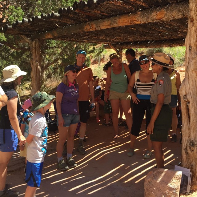 Ranger laughs and chats with visitors under a rustic shade shelter