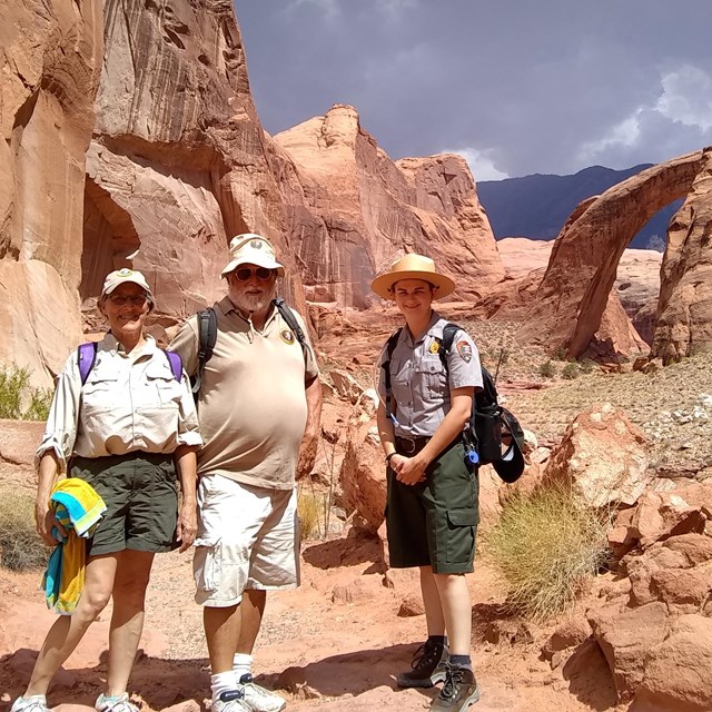 Ranger and two volunteers pause on trail with Rainbow Bridge in background