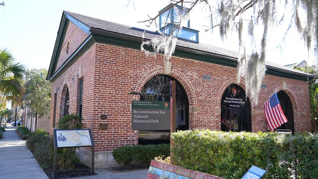 The visitor center of Reconstruction Era NHP, a brick single-story building with arched windows.
