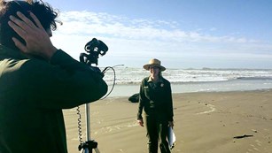 Two rangers on a beach film a video program.