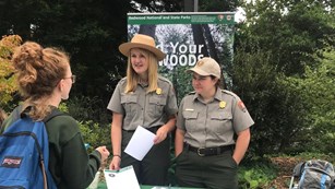 Two female rangers talk to a young adult at an event.