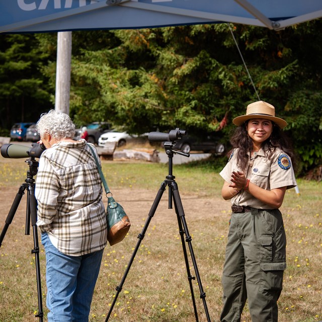 A California State Park employee smiling next to a large monocular.