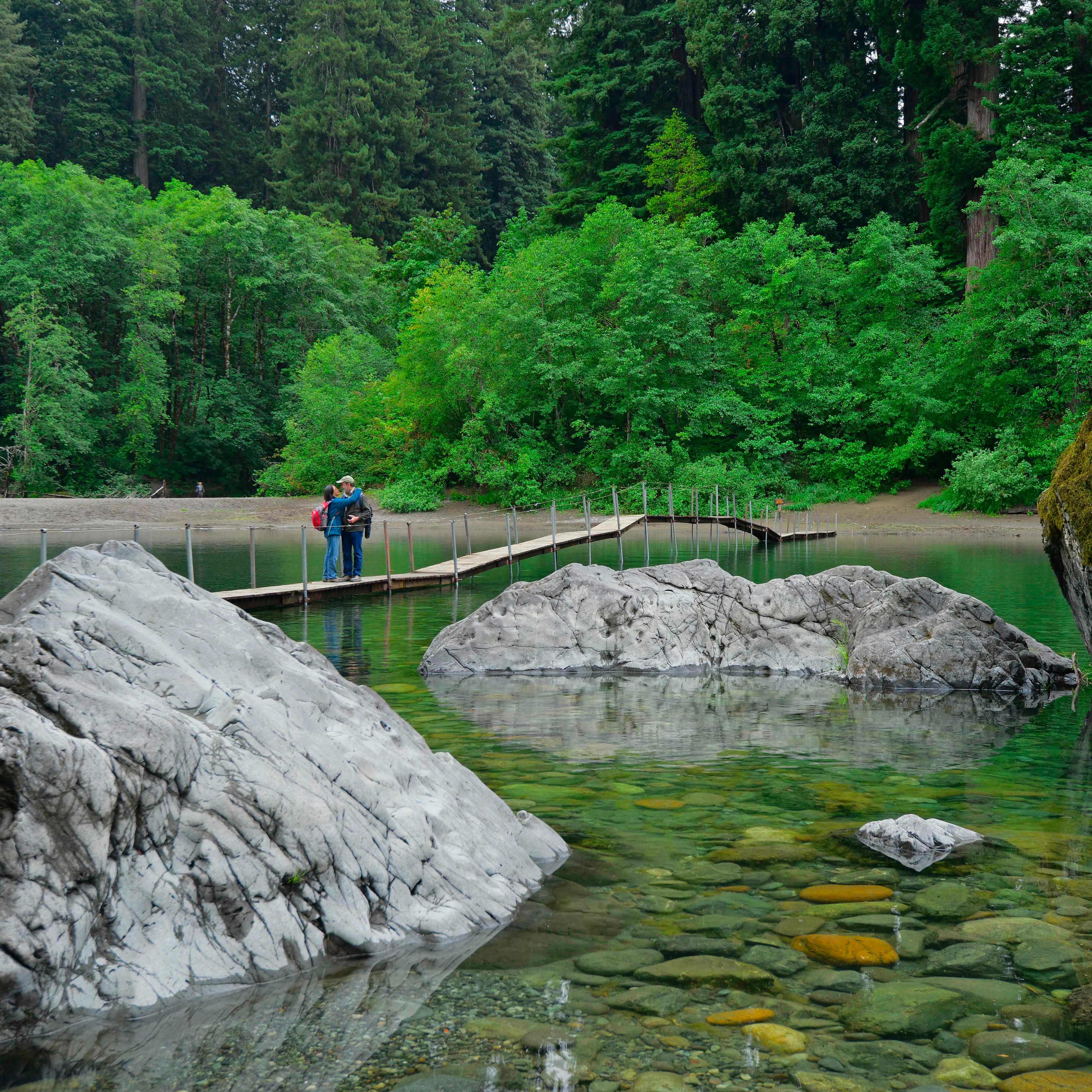 People walk across a wooden footbridge across a river