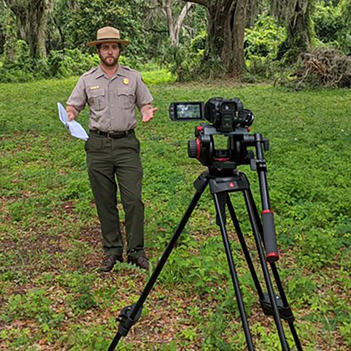A ranger stands behind a camera.