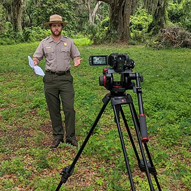 A ranger stands behind a camera.