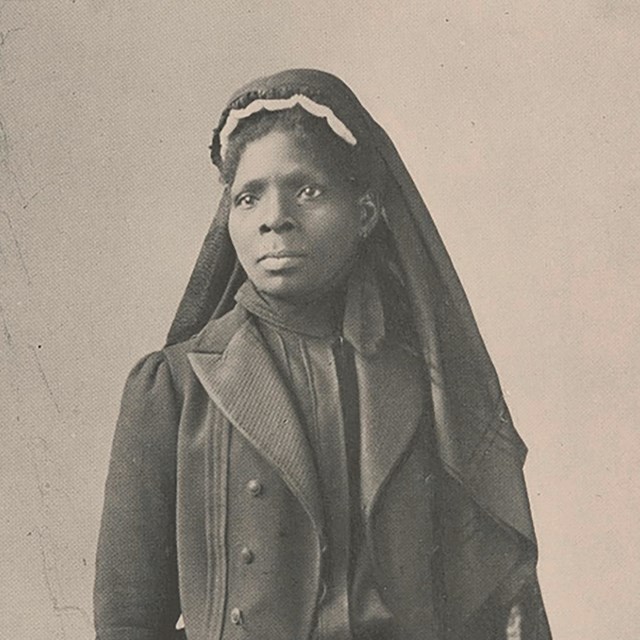 Susie King Taylor wears a nurse's outfit of a black skirt, shirt, jacket, and habit.