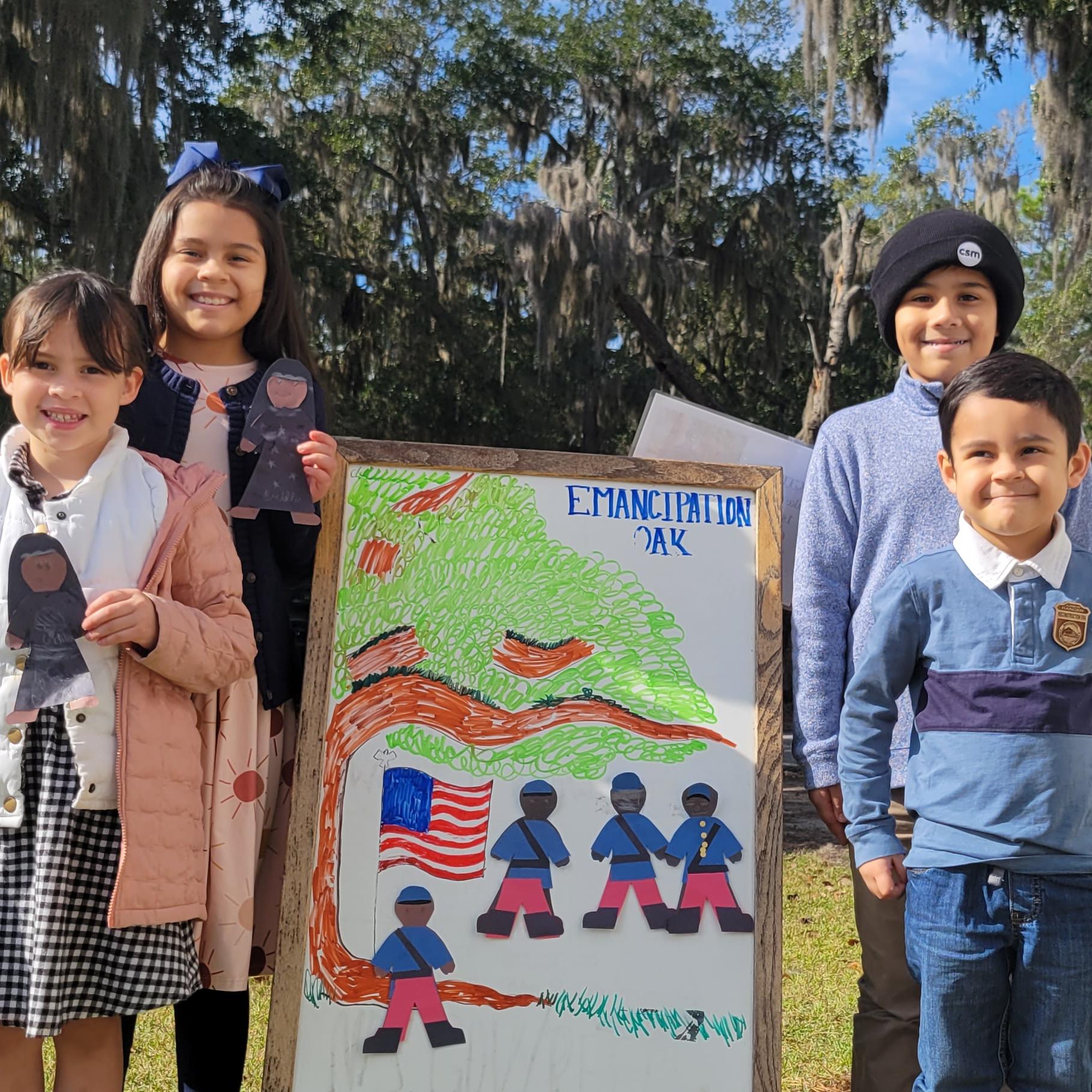 Four kids stand with paper nurses and soldiers they made wearing junior ranger badges.
