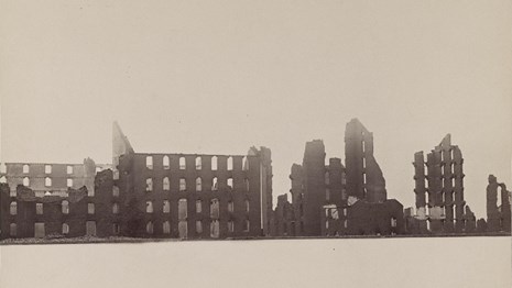 A black and white photograph of the collapsed ruins of brick buildings.
