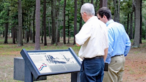 a photograph of two men examining a wayside side outdoors.