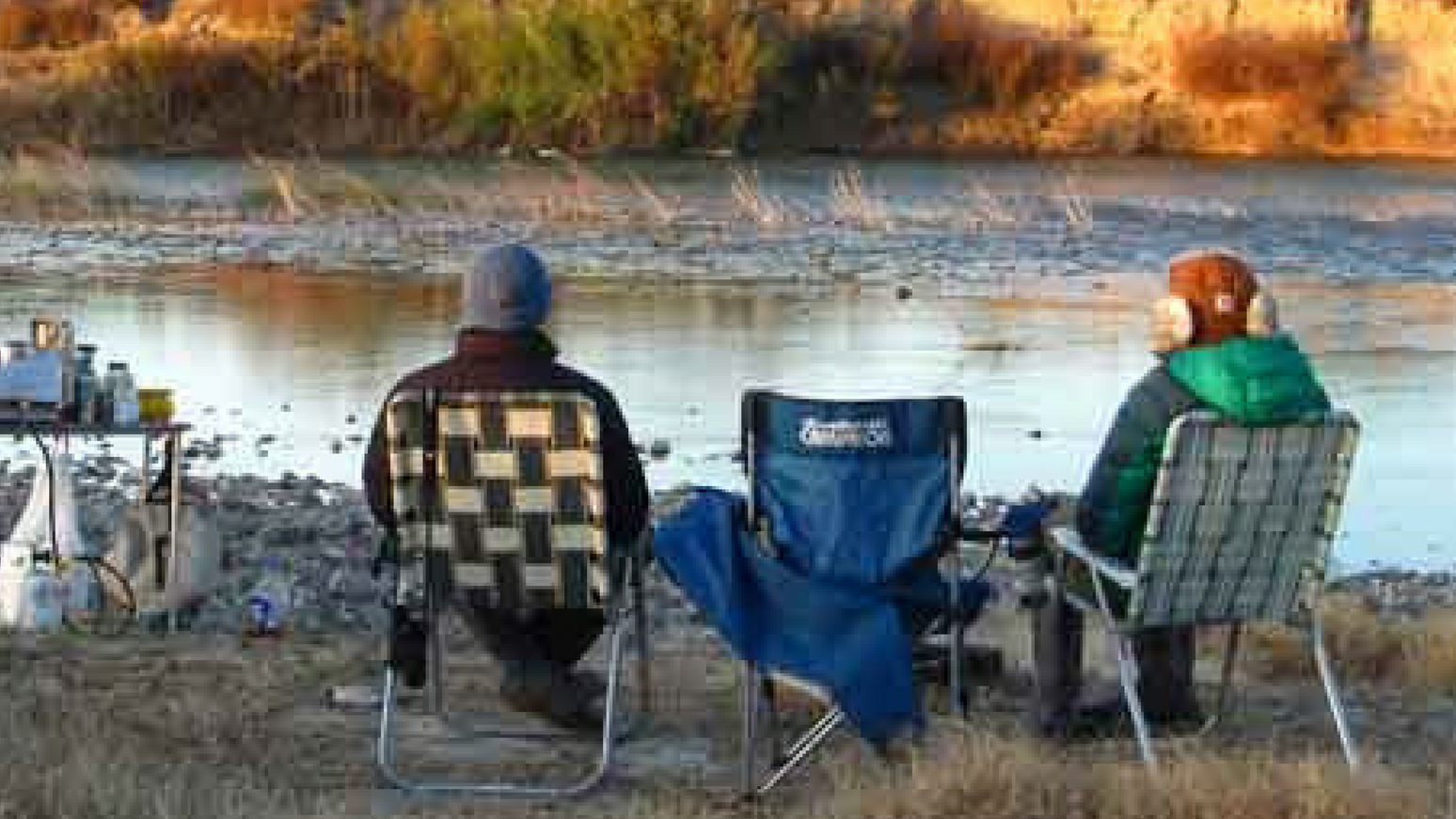 People sitting on chairs in front of a river.