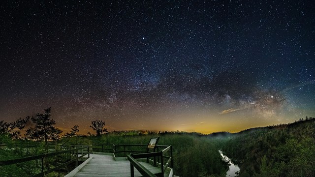 the milky way and stars over a boardwalk and a stream