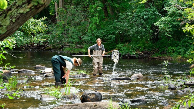 two people wearing waders sample the water of a flowing river