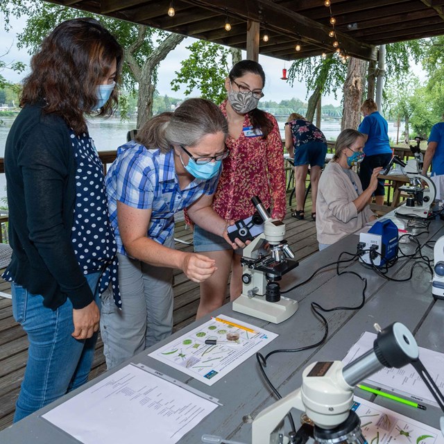 Students in face masks gather around microscopes in a floating classroom