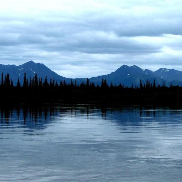 Blue sky, blue mountains, and blue water make the spruce trees and their reflection.