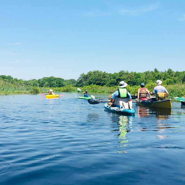 A group of people float in kayaks and canoes on a calm river