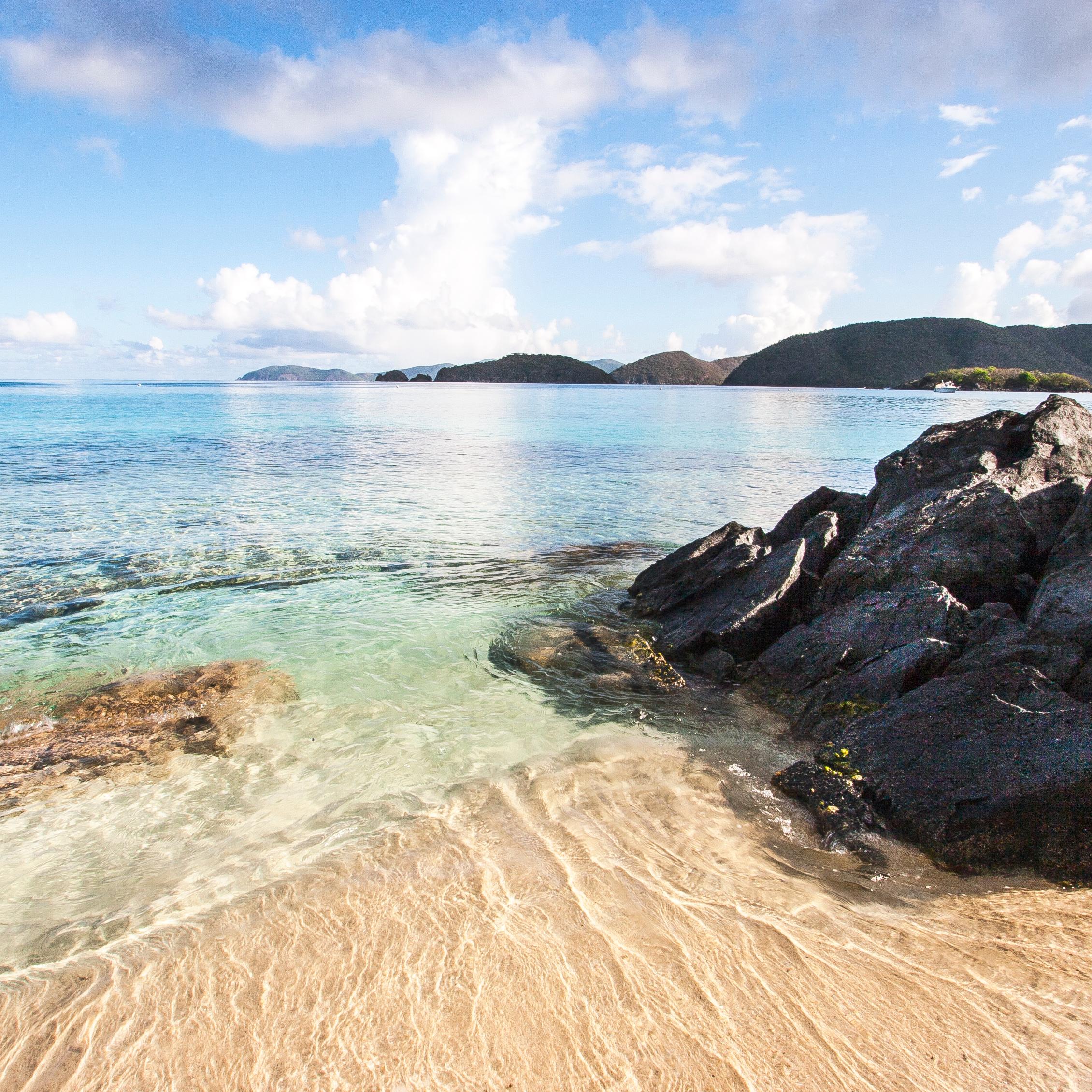 tropical blue ocean water laps arounds black rock and beach