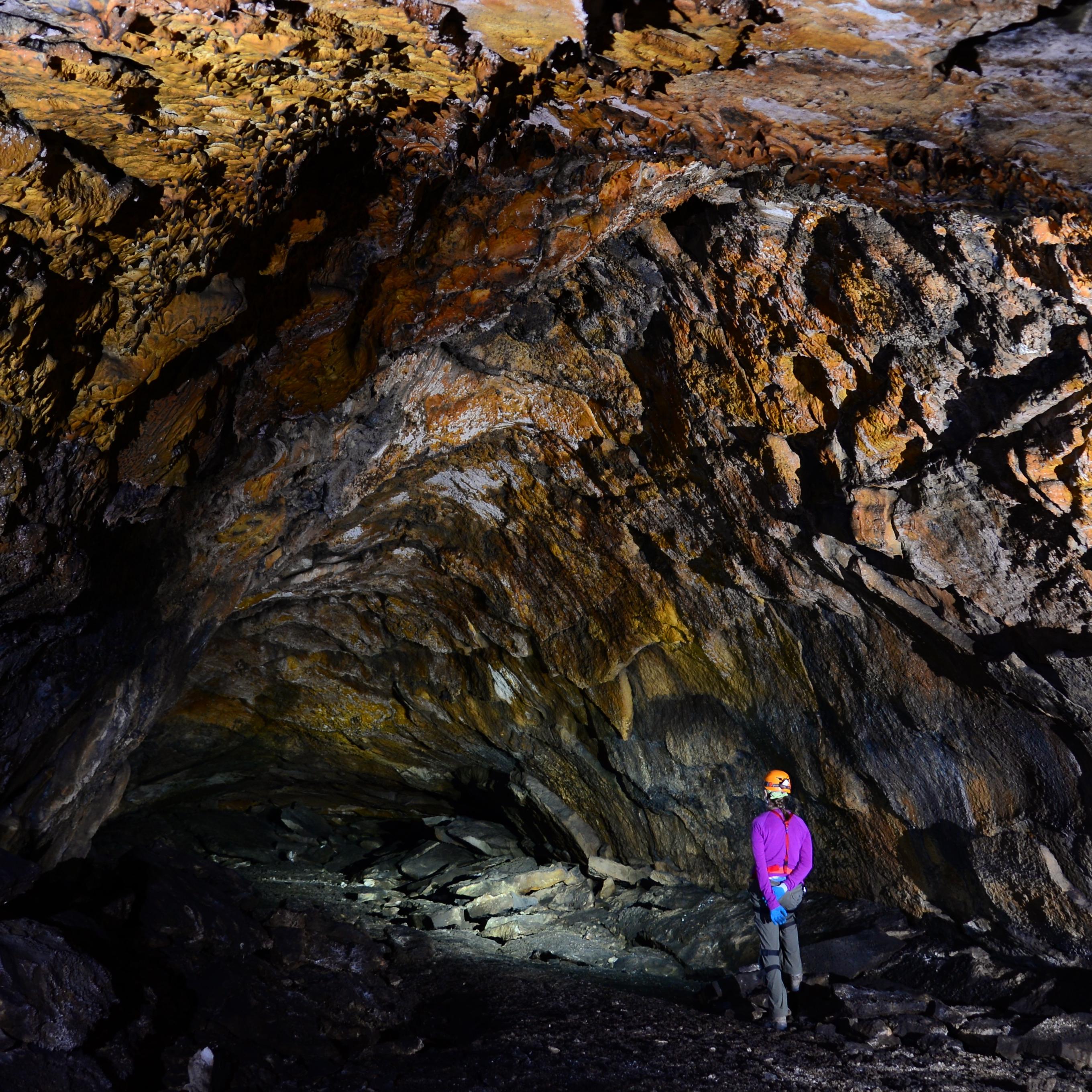 woman on right stands looking back at cave