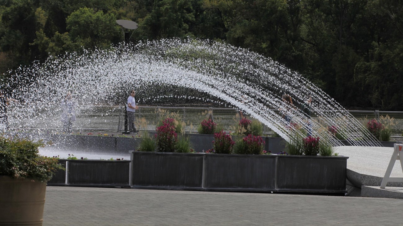 A fountain sprays water into the air over a smooth marble splash pad