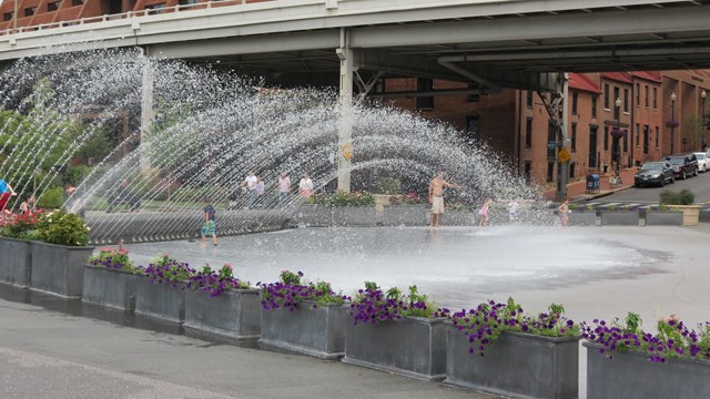 A fountain sprays water into the air over a smooth marble splash pad