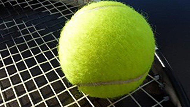 a yellow tennis ball rests on the head of a tennis racket