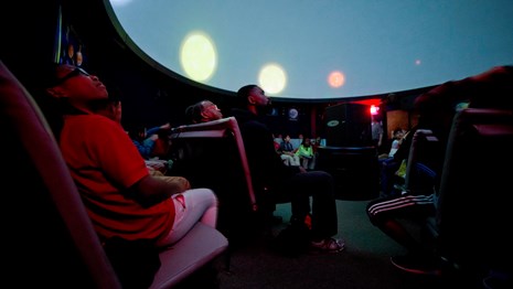 A child sitting with a crowd of people stares up at at the planetarium ceiling during a program.