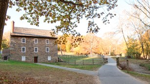Paved path stretches towards yellow leafed trees. A three story stone building sits just off center
