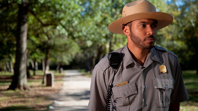 A ranger on a sidewalk through a park.