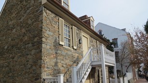 A two story stone house with small porch leading to door on second floor.