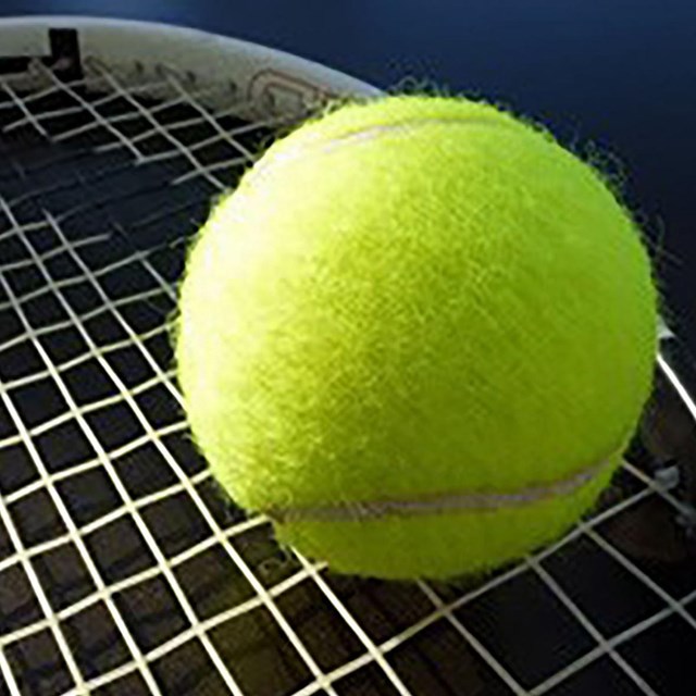 a yellow tennis ball rests on the head of a tennis racket