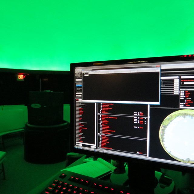 A computer monitor with the planetarium dome lit up with green light.