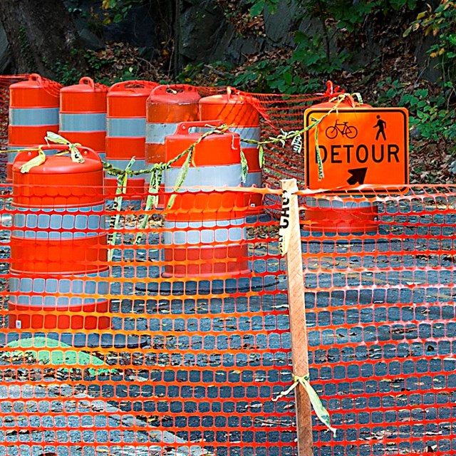 A road has bright orange barrels blocking the way. 