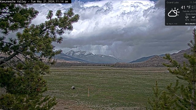 Webcam image of the Kawuneeche Valley, with green grasses and storm clouds overhead