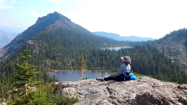 A hiker is sitting on a rock and overlooking an alpine lake
