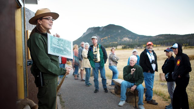 A park ranger is leading a program and holding up photos to a group of park visitors