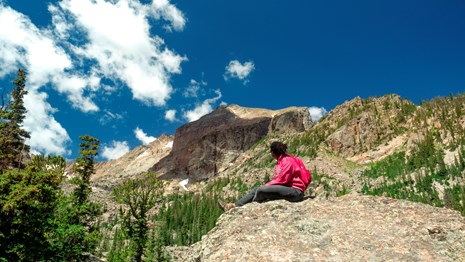 A visitor is sitting on a rock in summer and looking at the sky